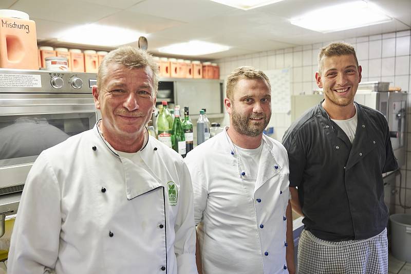 The chef and two employees stand happily in the kitchen