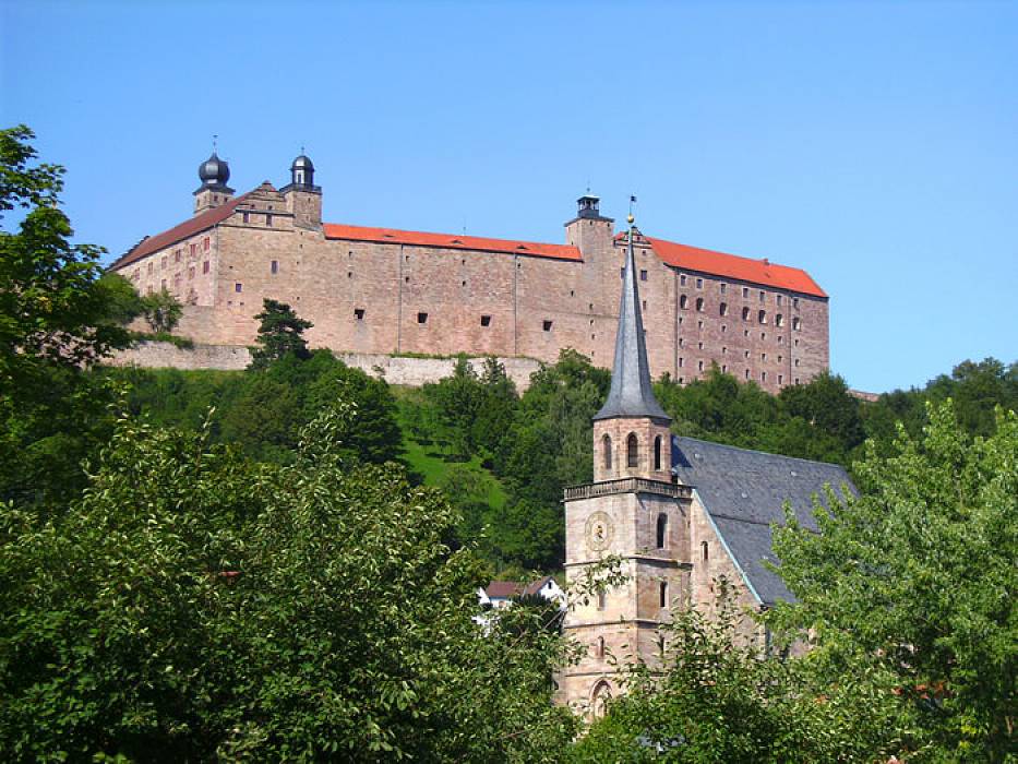 A photo of Kulmbach Plassenburg castle high above Kulmbach surrounded by green trees [[source: 'Source: City of Kulmbach']]