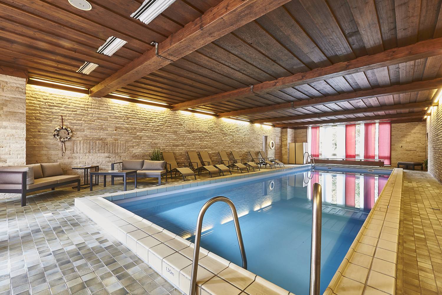 Light-flooded indoor swimming pool with sunbeds, tables and benches