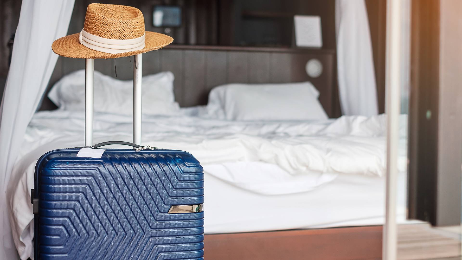 Blauer Koffer mit Hut im modernen Hotelzimmer